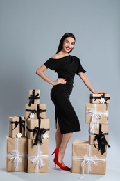 Photo of Woman in black dress with Christmas gifts on grey background