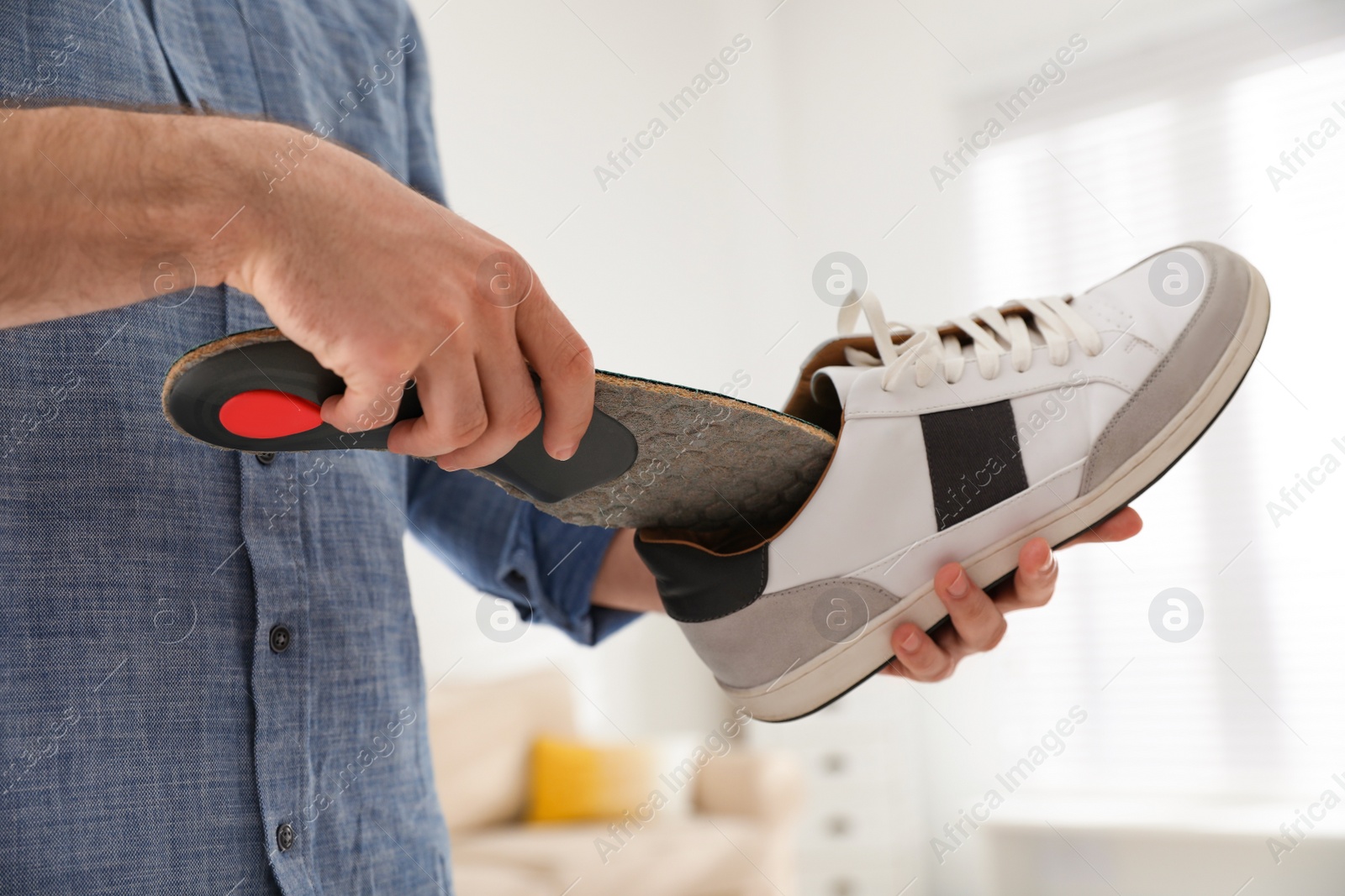 Photo of Man putting orthopedic insole into shoe at home, closeup