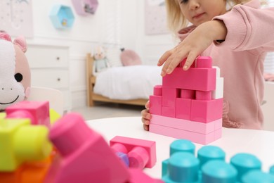 Cute little girl playing with colorful building blocks at table in room, closeup. Space for text