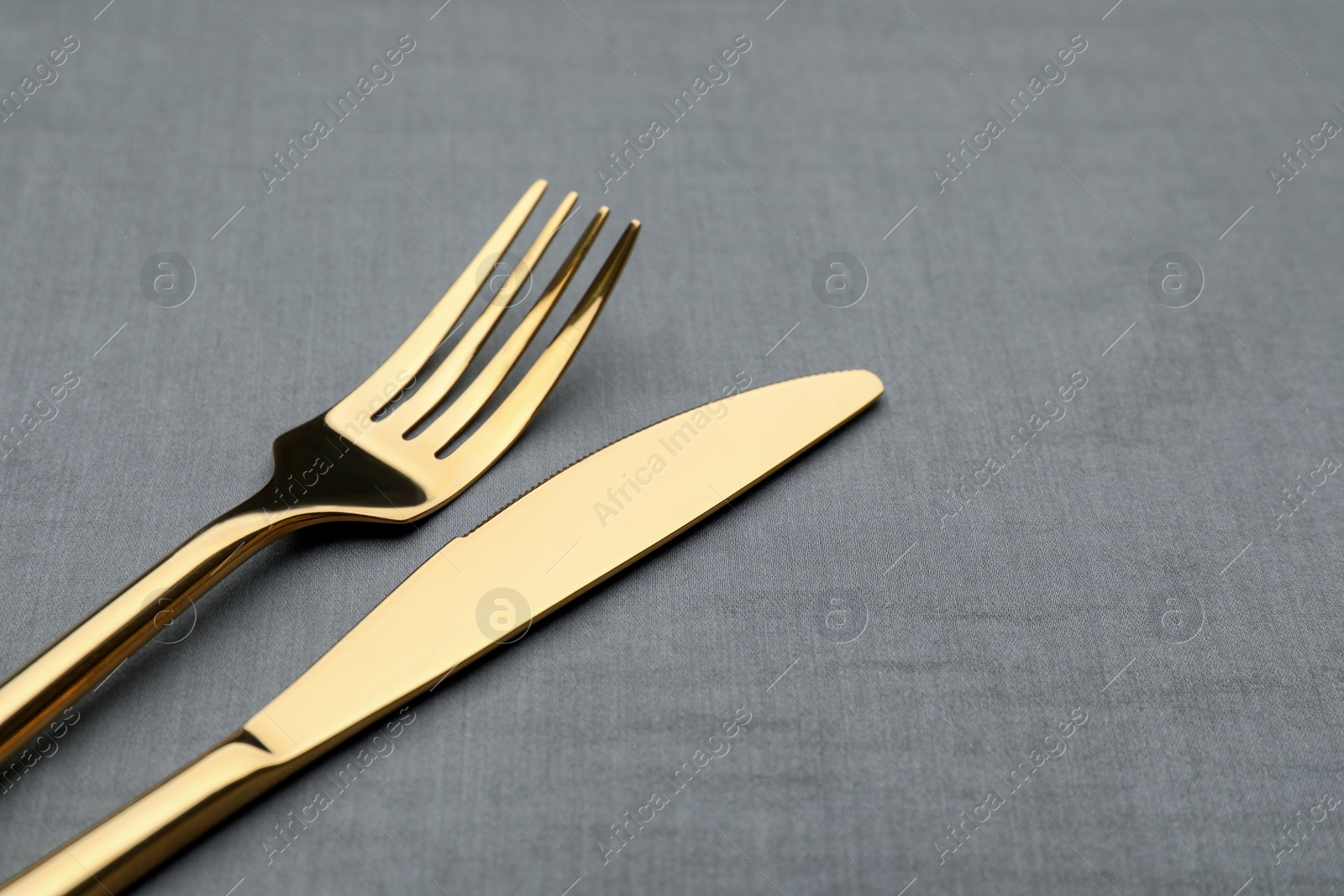 Photo of Golden fork and knife on grey table, closeup. Space for text