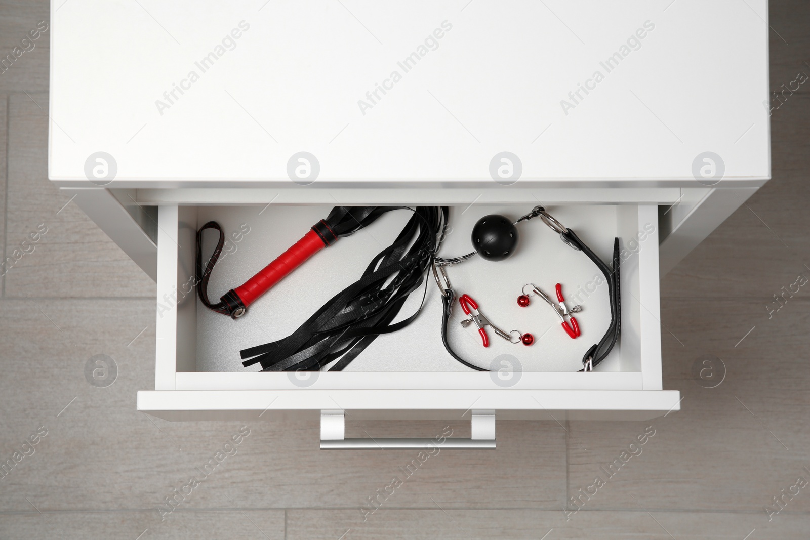 Photo of Black ball gag, whip and nipple clamps in drawer indoors, top view. Sex toys