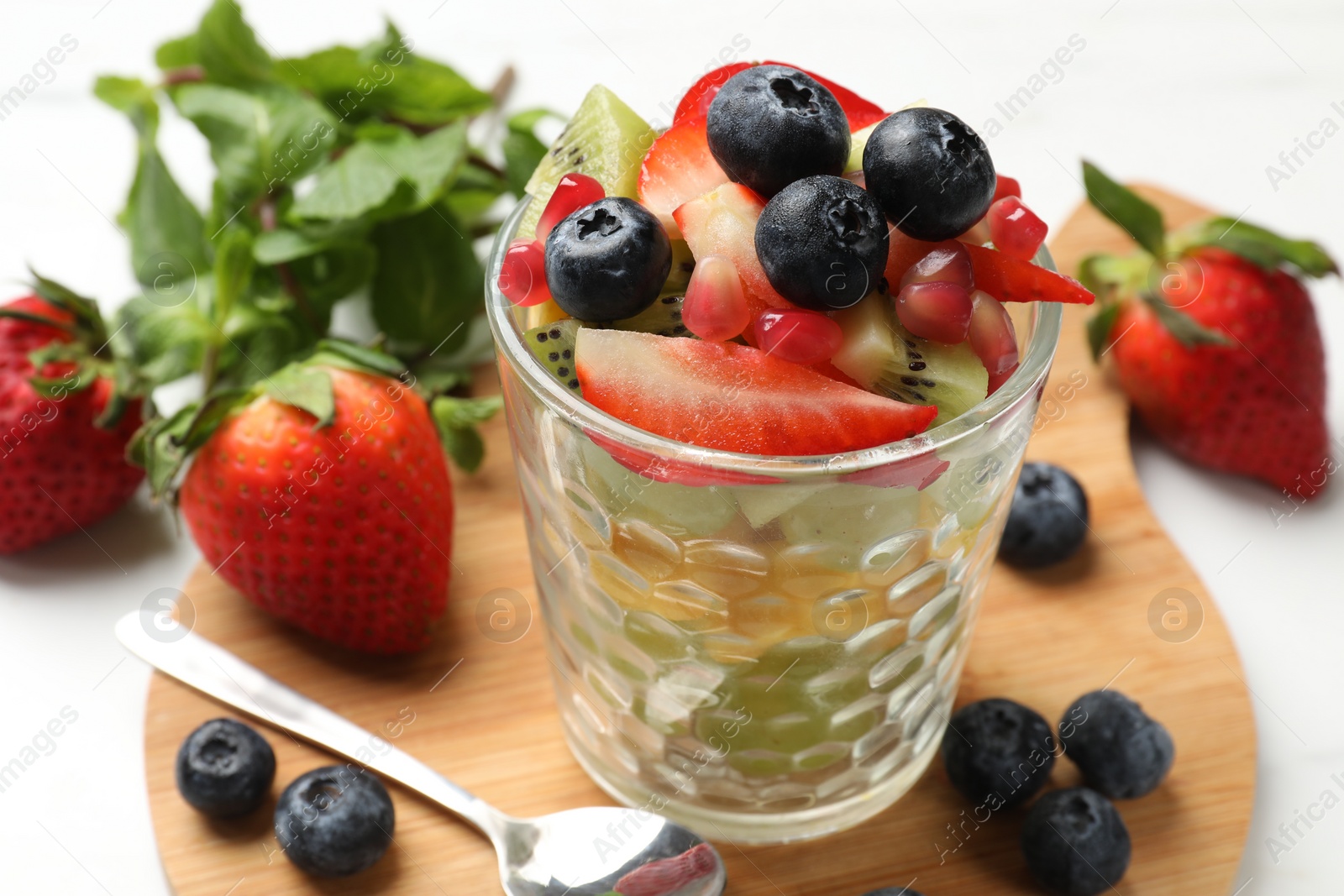 Photo of Healthy breakfast. Delicious fruit salad in glass and ingredients on white table, closeup