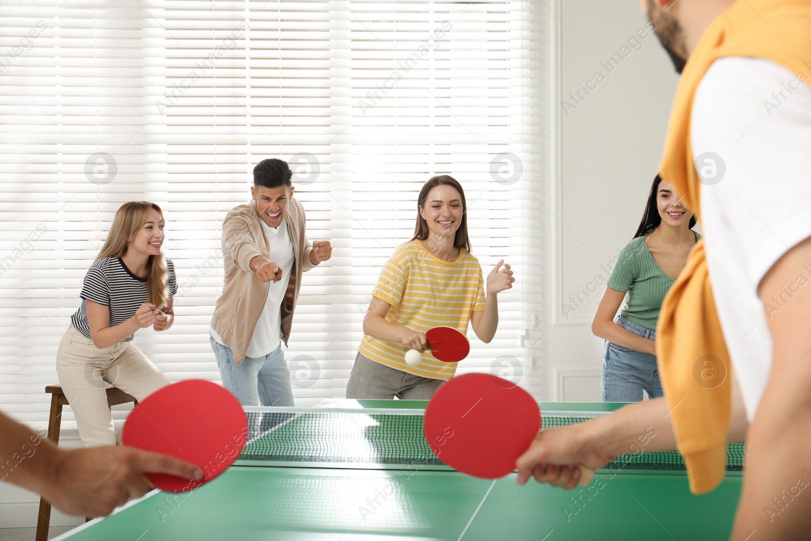 Photo of Happy friends playing ping pong together indoors