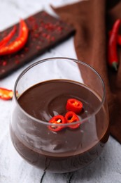 Photo of Glass of hot chocolate with chili pepper on white textured table, closeup