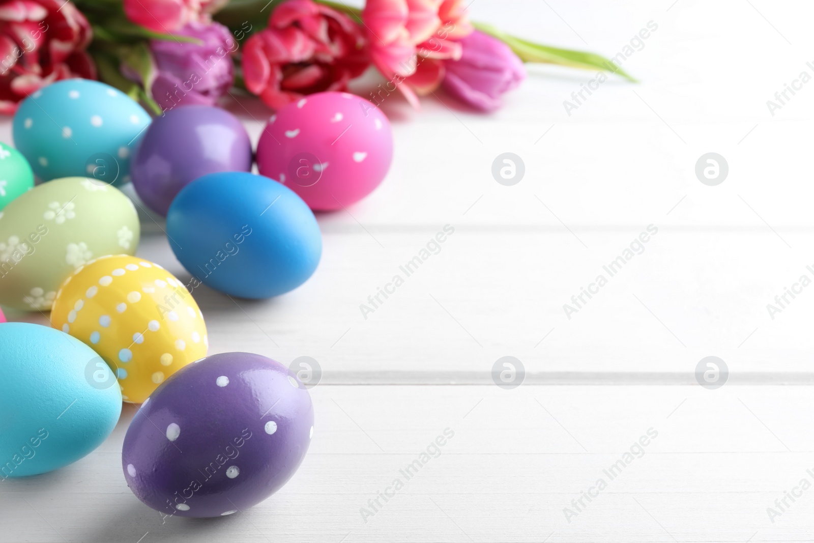 Photo of Colorful eggs and tulips on white wooden background, space for text. Happy Easter