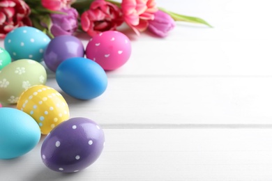 Colorful eggs and tulips on white wooden background, space for text. Happy Easter