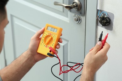 Photo of Professional electrician with tester checking light switch voltage indoors, closeup