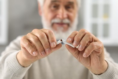 Photo of Stop smoking concept. Senior man breaking cigarette indoors, selective focus