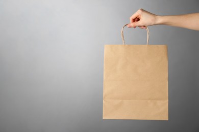 Woman holding kraft paper bag on grey background, closeup with space for text. Mockup for design