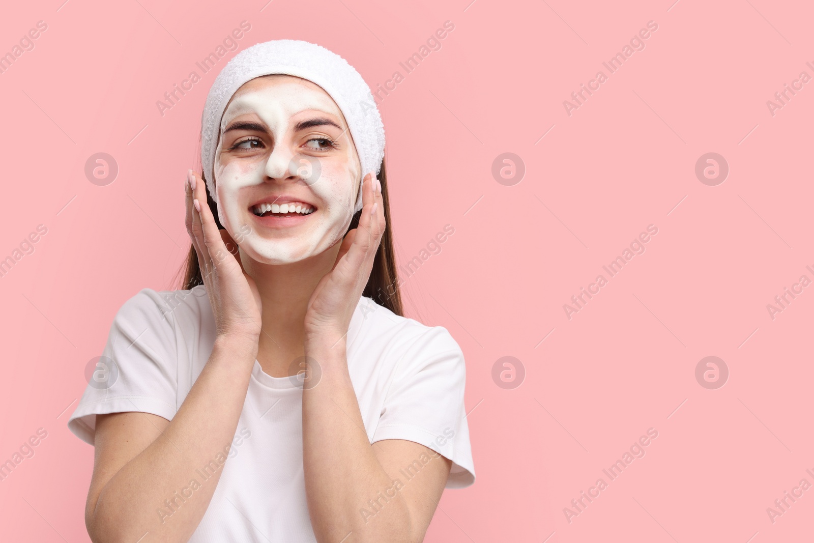 Photo of Young woman with headband washing her face on pink background, space for text