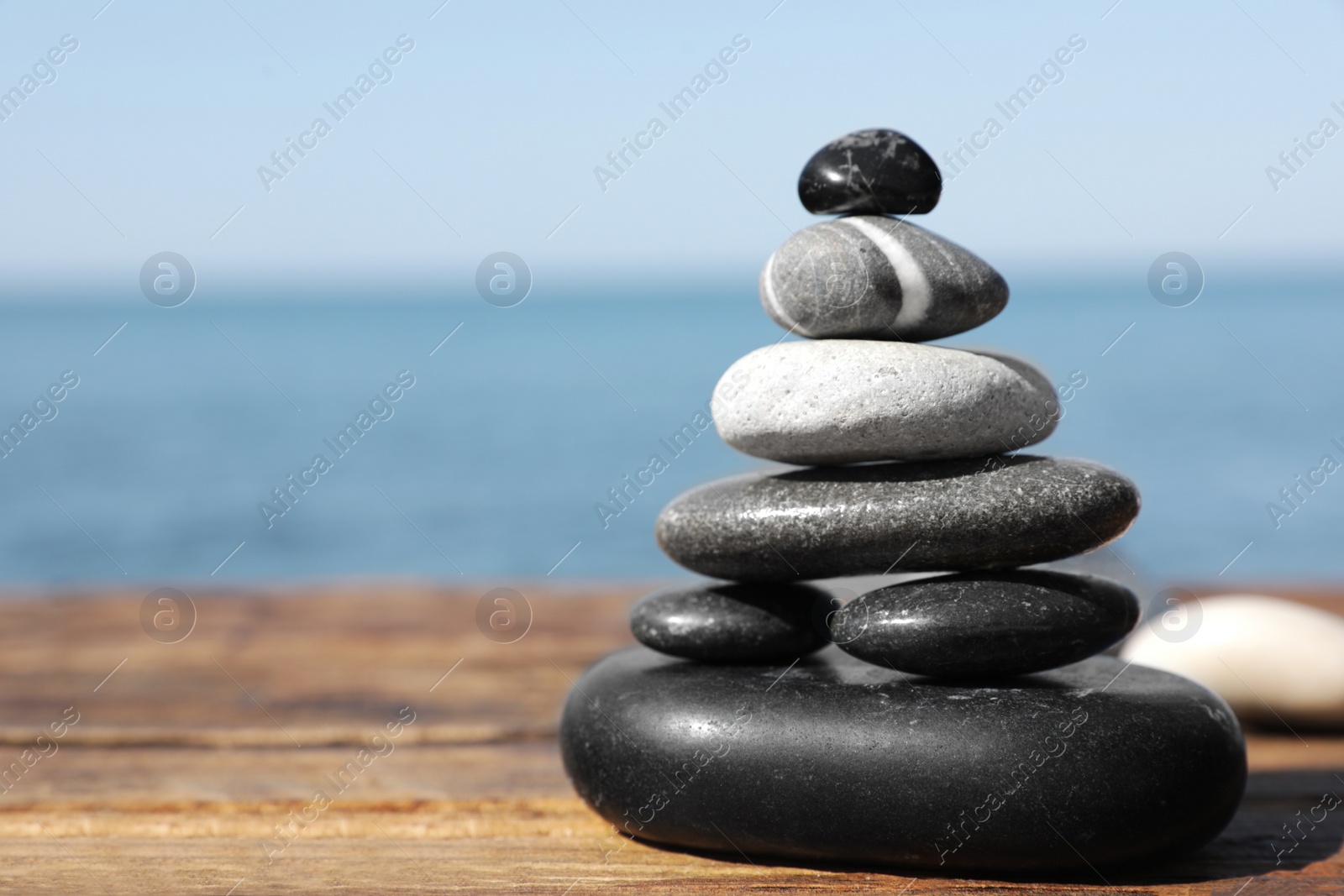 Photo of Stack of stones on wooden pier near sea seascape, space for text. Zen concept