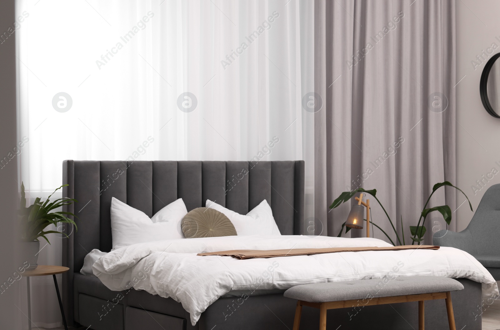 Photo of Stylish bedroom interior with large bed, ottoman, lamp and houseplants