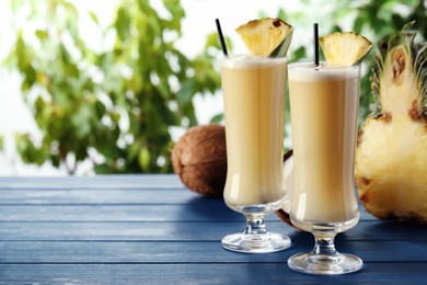 Photo of Tasty Pina Colada cocktails and ingredients on light blue wooden table, space for text