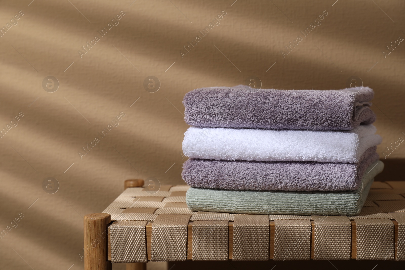 Photo of Stacked terry towels on wicker bench near beige wall, space for text