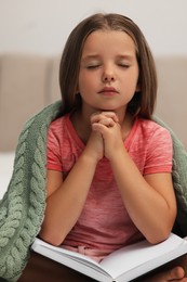 Photo of Cute little girl praying over Bible in bedroom