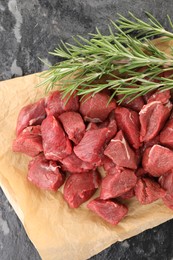 Photo of Pieces of raw beef meat and rosemary on grey textured table, top view