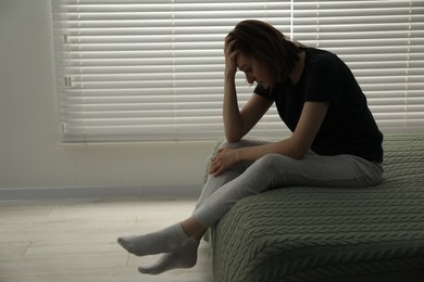 Sad young woman sitting on bed at home, space for text