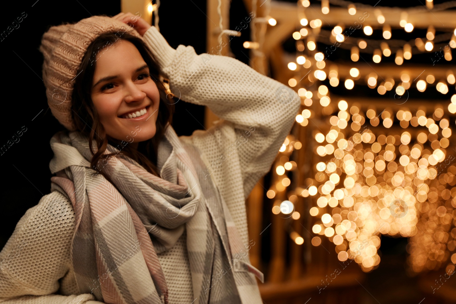 Photo of Young woman wearing warm sweater, hat and scarf  outdoors at night. Winter season