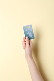 Woman holding credit card on pale yellow background, closeup