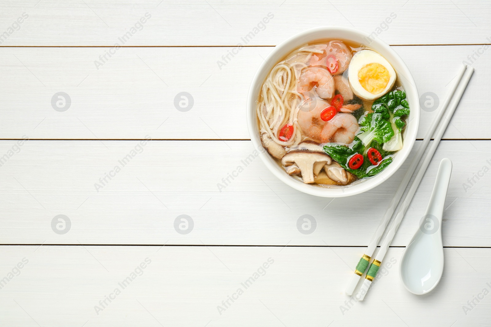 Photo of Tasty ramen with shrimps in bowl and chopsticks on white wooden table, top view. Space for text