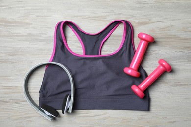 Photo of Stylish sports bra, dumbbells and headphones on wooden background, flat lay