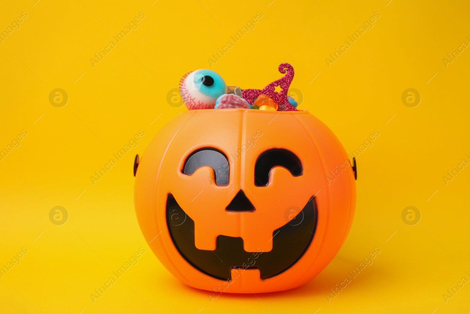 Photo of Halloween trick or treat bucket with different sweets on yellow background