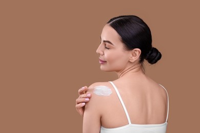 Photo of Beautiful woman with smear of body cream on her shoulder against light brown background, space for text