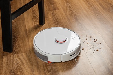 Photo of Robotic vacuum cleaner removing dirt from wooden floor indoors