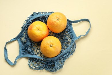Photo of String bag with oranges on beige background, top view