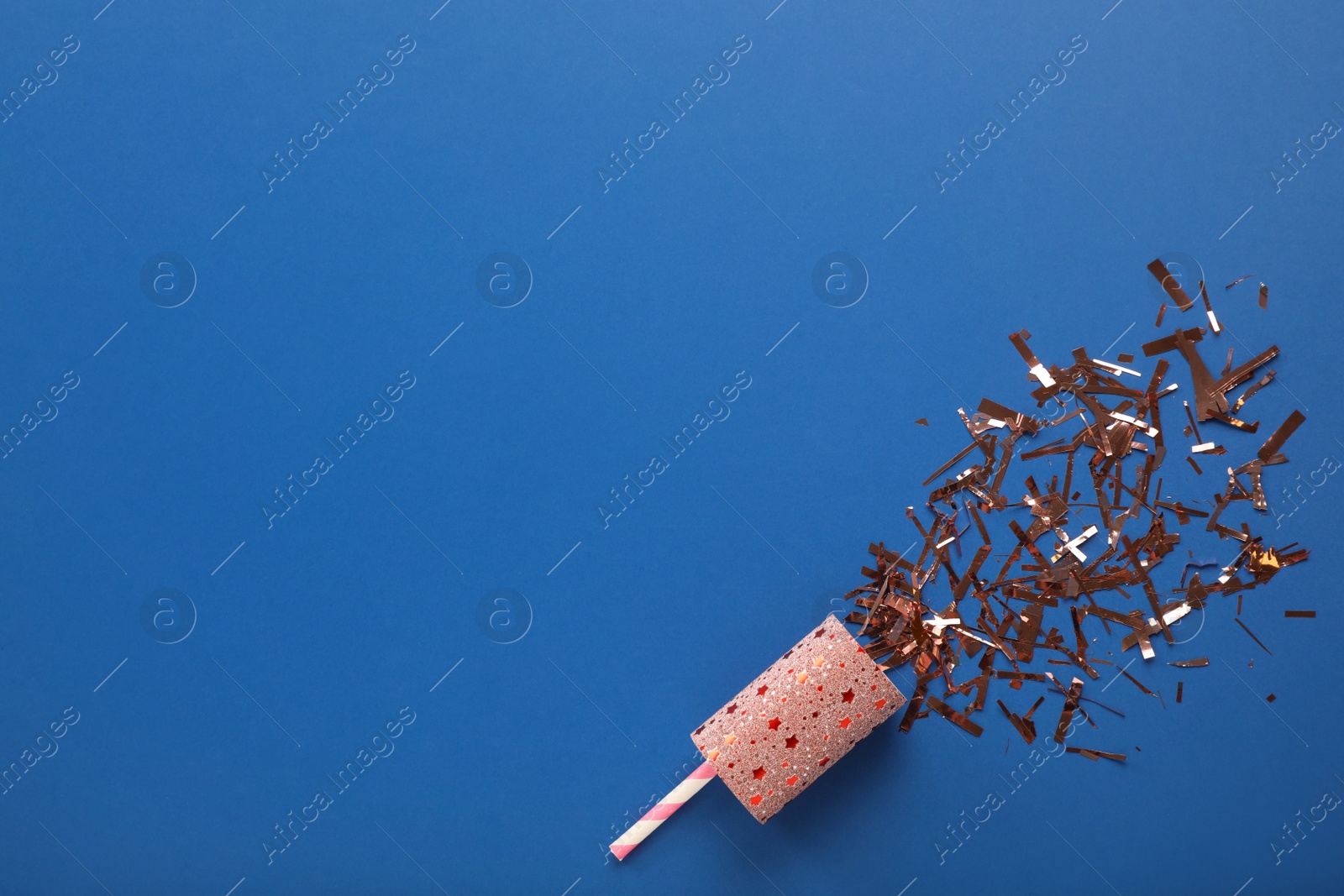 Photo of Confetti with party cracker on blue background, top view. Space for text