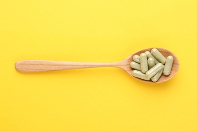 Photo of Vitamin pills in wooden spoon on yellow background, top view
