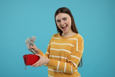 Woman putting money into wallet on light blue background