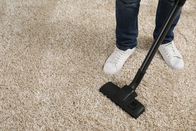 Man cleaning carpet with vacuum cleaner at home, closeup. Space for text