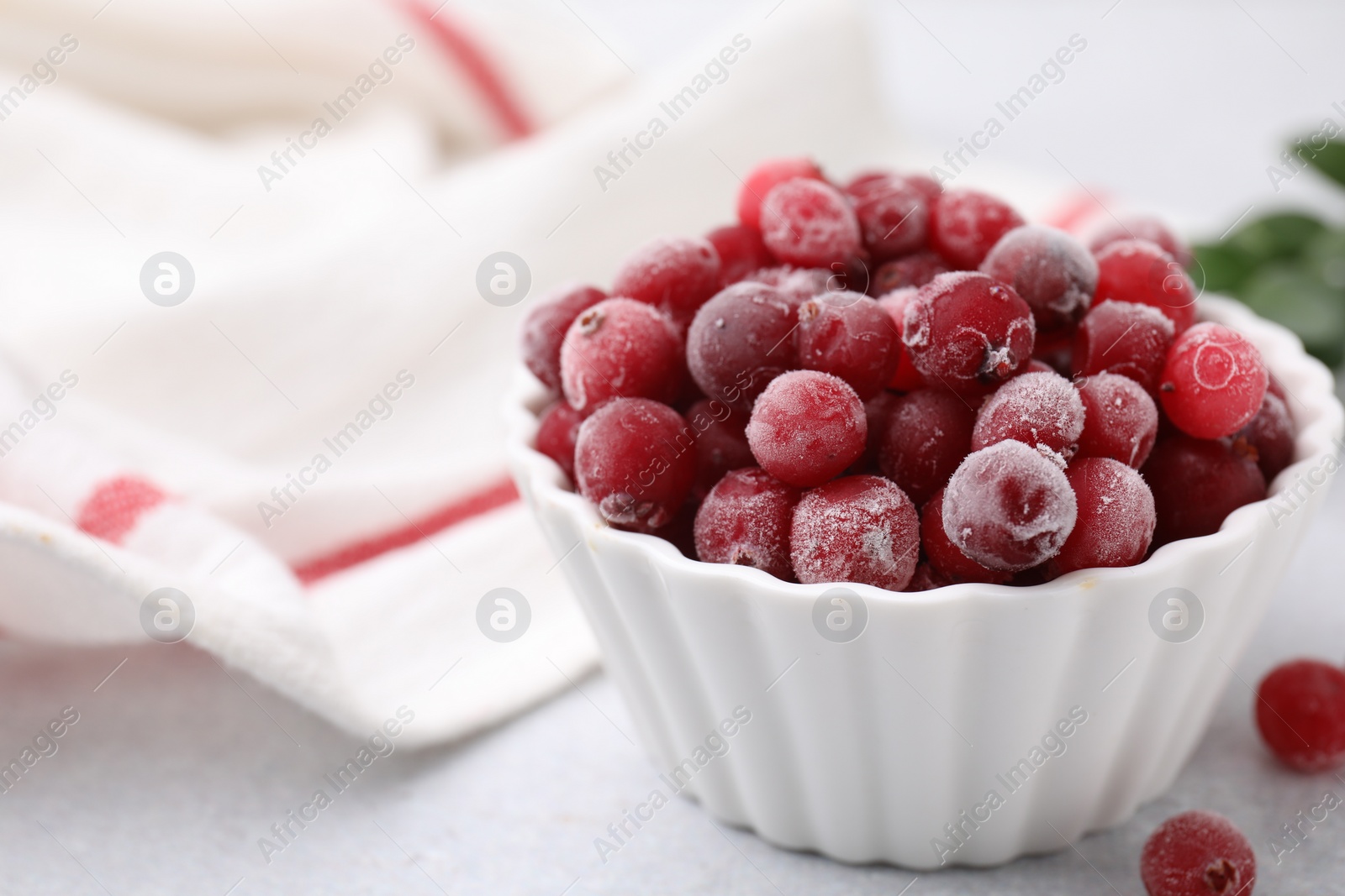 Photo of Frozen red cranberries in bowl on light table, closeup. Space for text