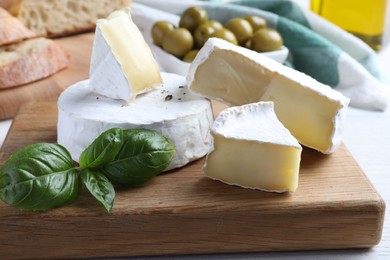 Photo of Tasty brie cheese with basil on wooden board, closeup