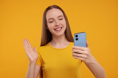 Photo of Happy young woman using smartphone and having video chat on yellow background