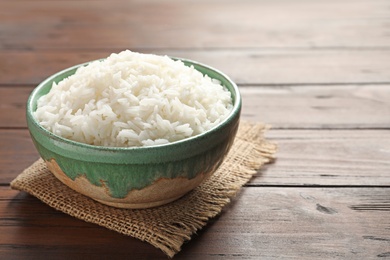 Photo of Bowl of tasty cooked white rice on wooden table. Space for text