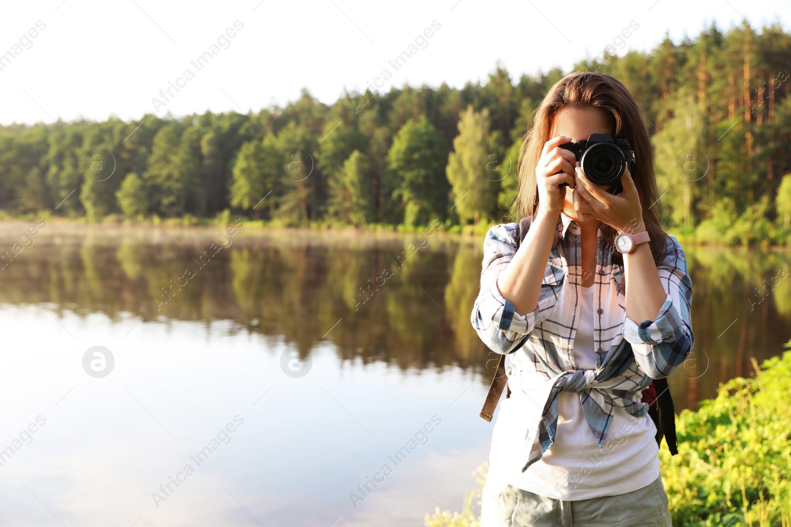 Photo of Young female photographer with camera on shore of lake. Camping season