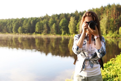 Young female photographer with camera on shore of lake. Camping season