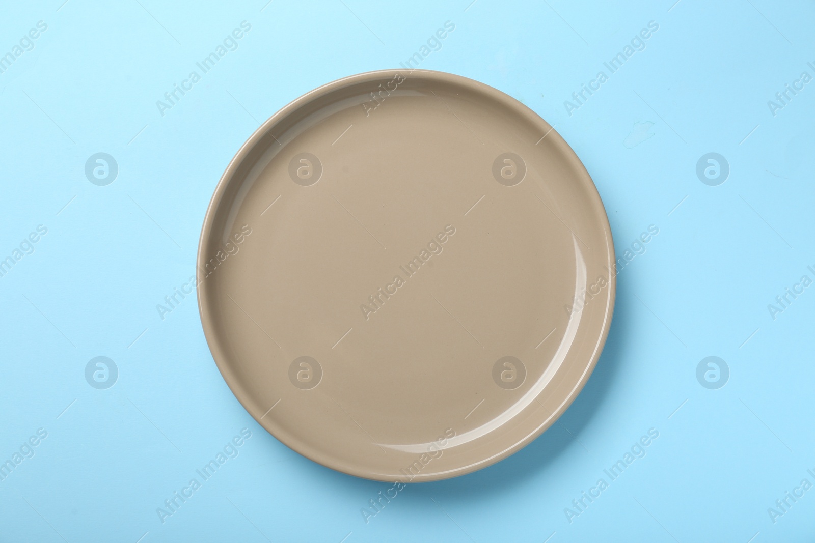 Photo of Empty beige ceramic plate on light blue background, top view
