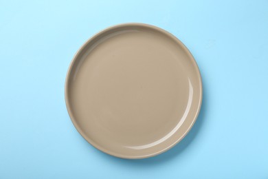 Empty beige ceramic plate on light blue background, top view