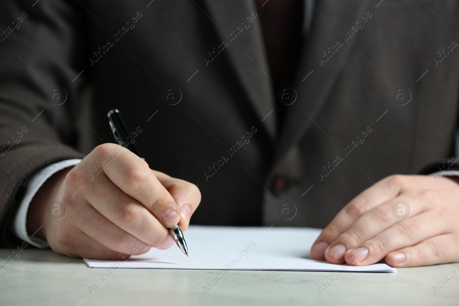 Photo of Man writing on sheet of paper with pen at white table, closeup