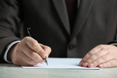Man writing on sheet of paper with pen at white table, closeup