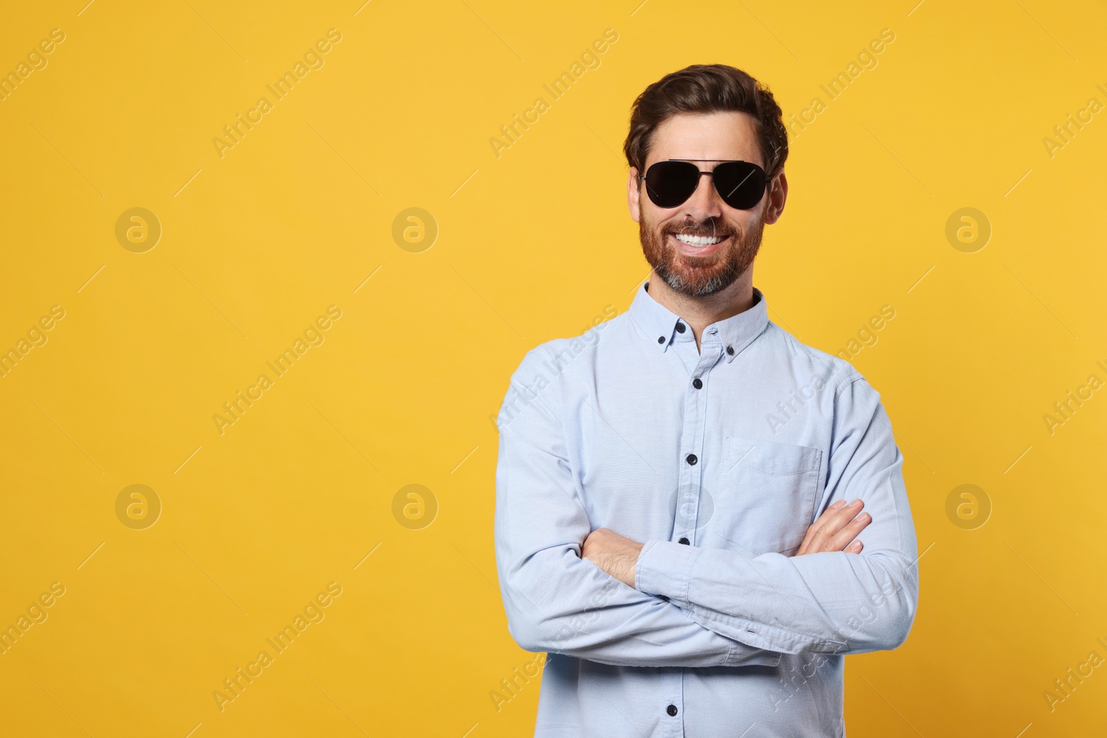 Photo of Portrait of smiling bearded man with stylish sunglasses on orange background. Space for text