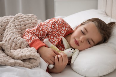 Photo of Cute little girl with toy bunny sleeping in bed at home