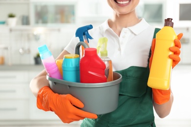 Photo of Woman with basin of detergents and bottle in kitchen, closeup. Cleaning service