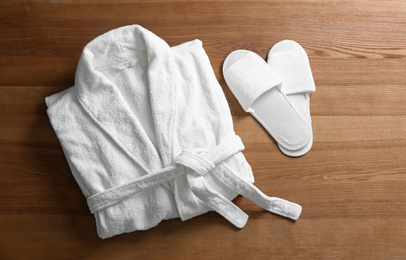 Photo of Clean folded bathrobe and slippers on wooden background, flat lay