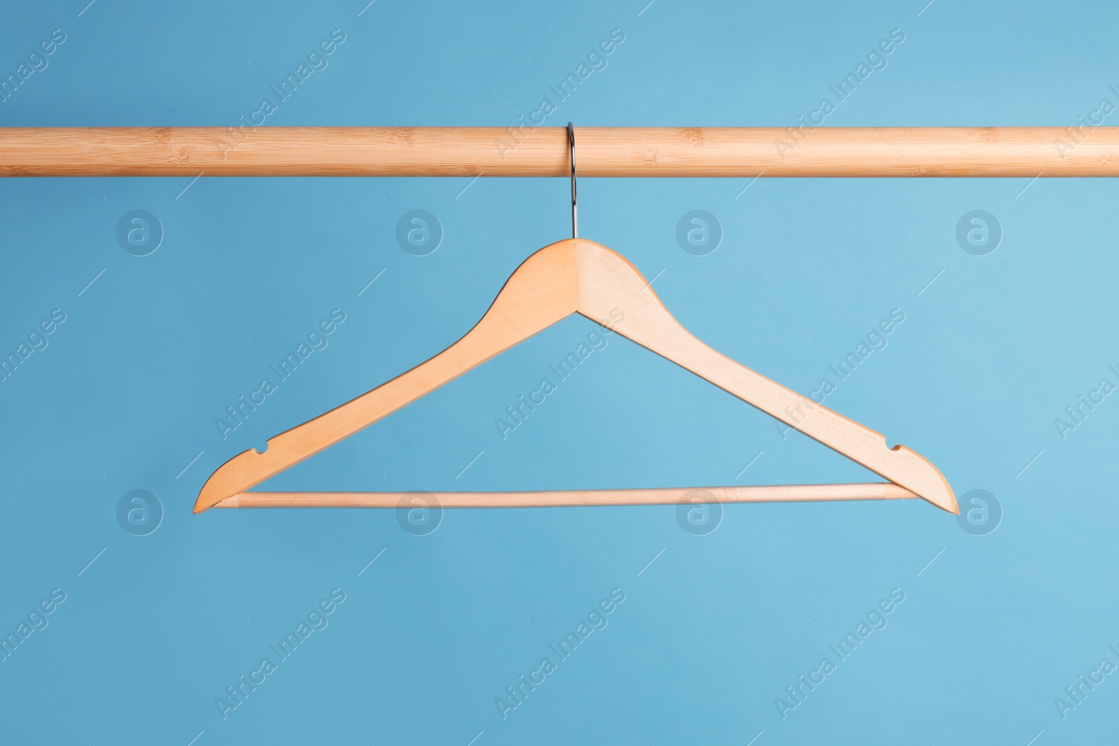 Photo of Empty clothes hanger on wooden rail against light blue background