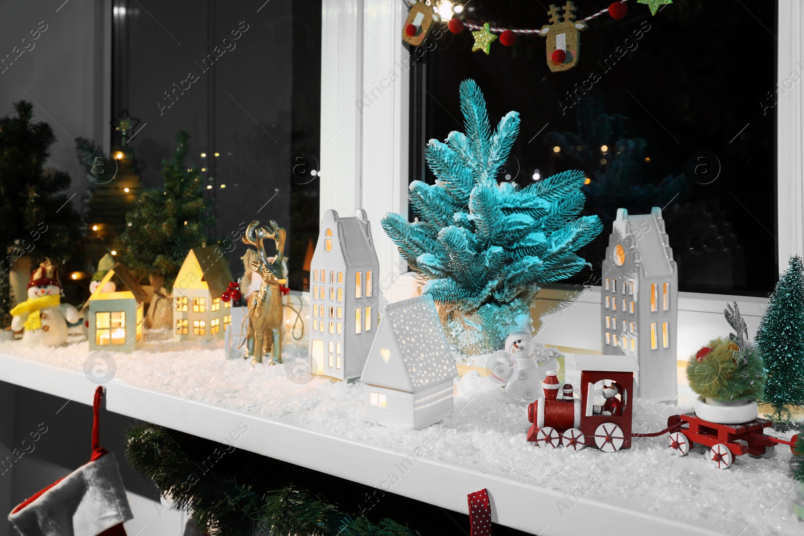 Photo of Christmas atmosphere. Beautiful glowing houses, fir trees, artificial snow and toys on window sill indoors