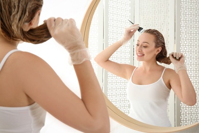 Photo of Young woman dyeing her hair in front of mirror at home